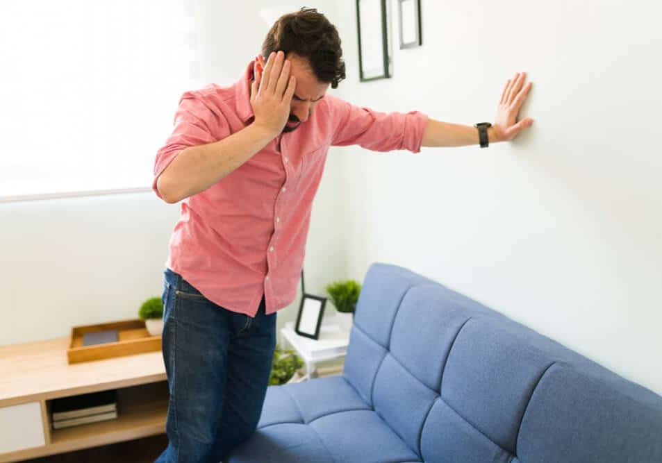 Disoriented man in his 30s feeling dizzy and trying to balance against a wall